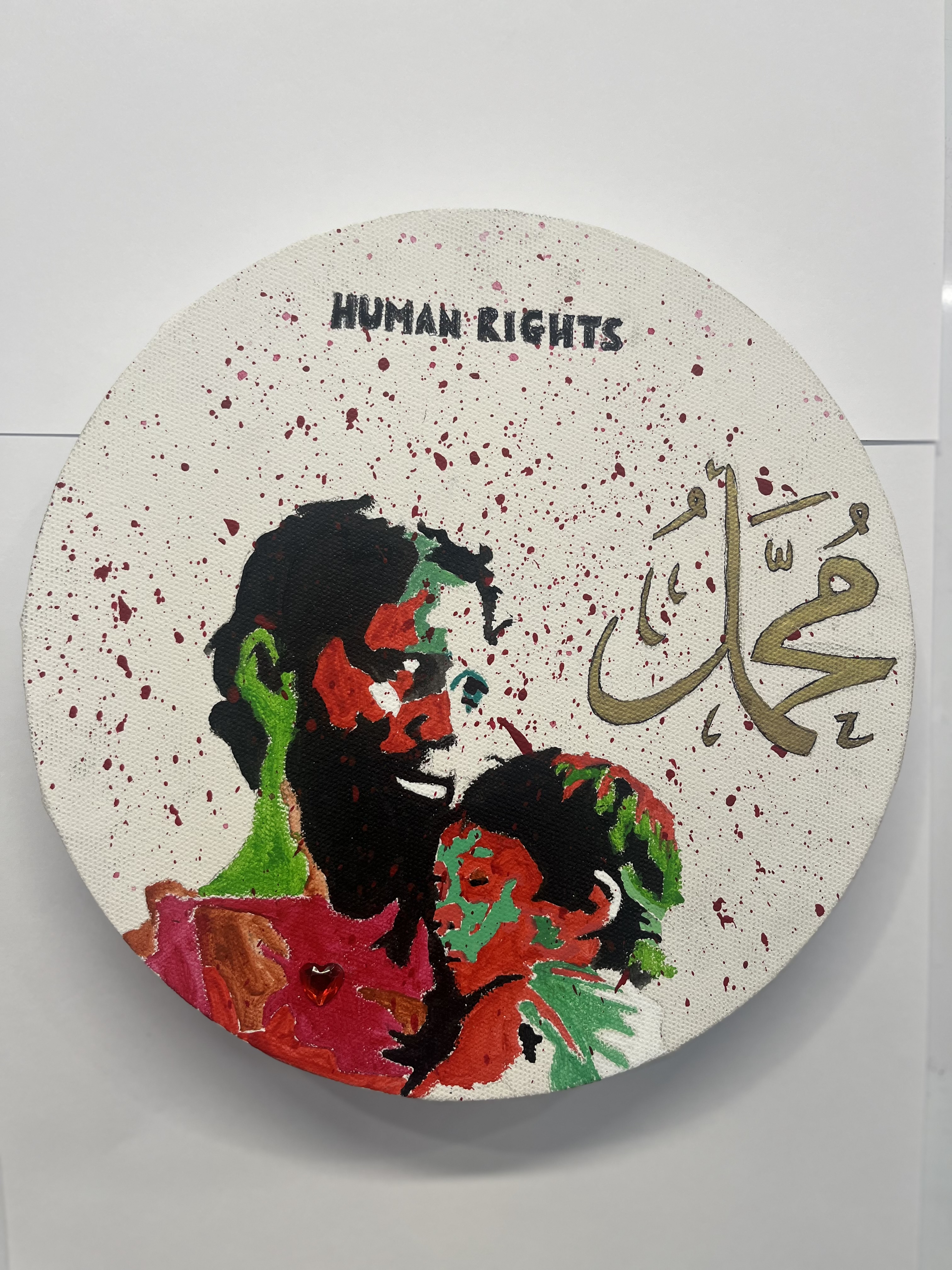 Round canvas painting depicting a father holding a child, with Arabic calligraphy, red splatter marks, and the text Human Rights, exploring themes of human rights and family
